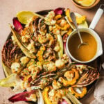 Roasted cauliflower, squash, and radicchio on a platter with a small pitcher of dressing and a bowl of lemon wedges.