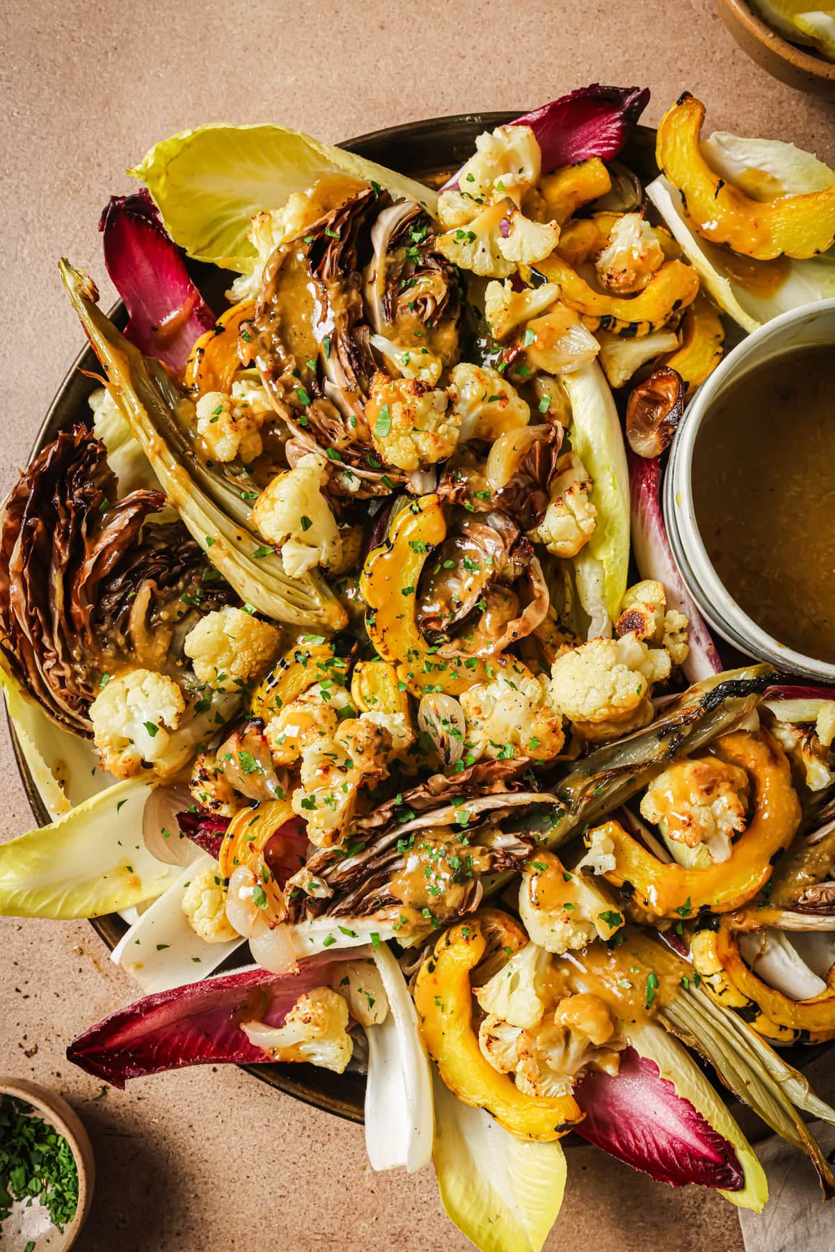 Roasted cauliflower, radicchio, and squash salad drizzled with dressing, served with a side of vinaigrette.
