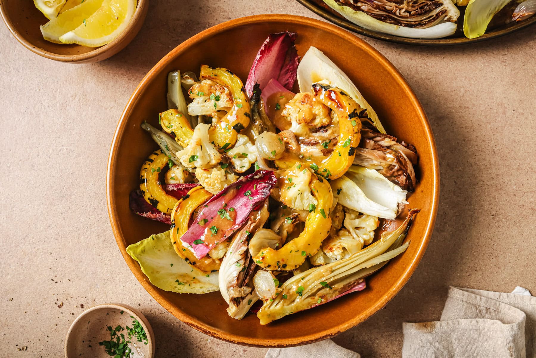 A bowl of roasted cauliflower and radicchio salad with yellow squash, topped with herbs and a glaze.