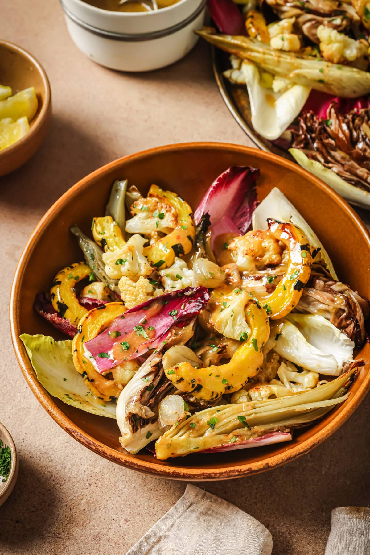A ceramic bowl filled with roasted cauliflower, delicata squash, and radicchio drizzled with herb-flecked dressing.