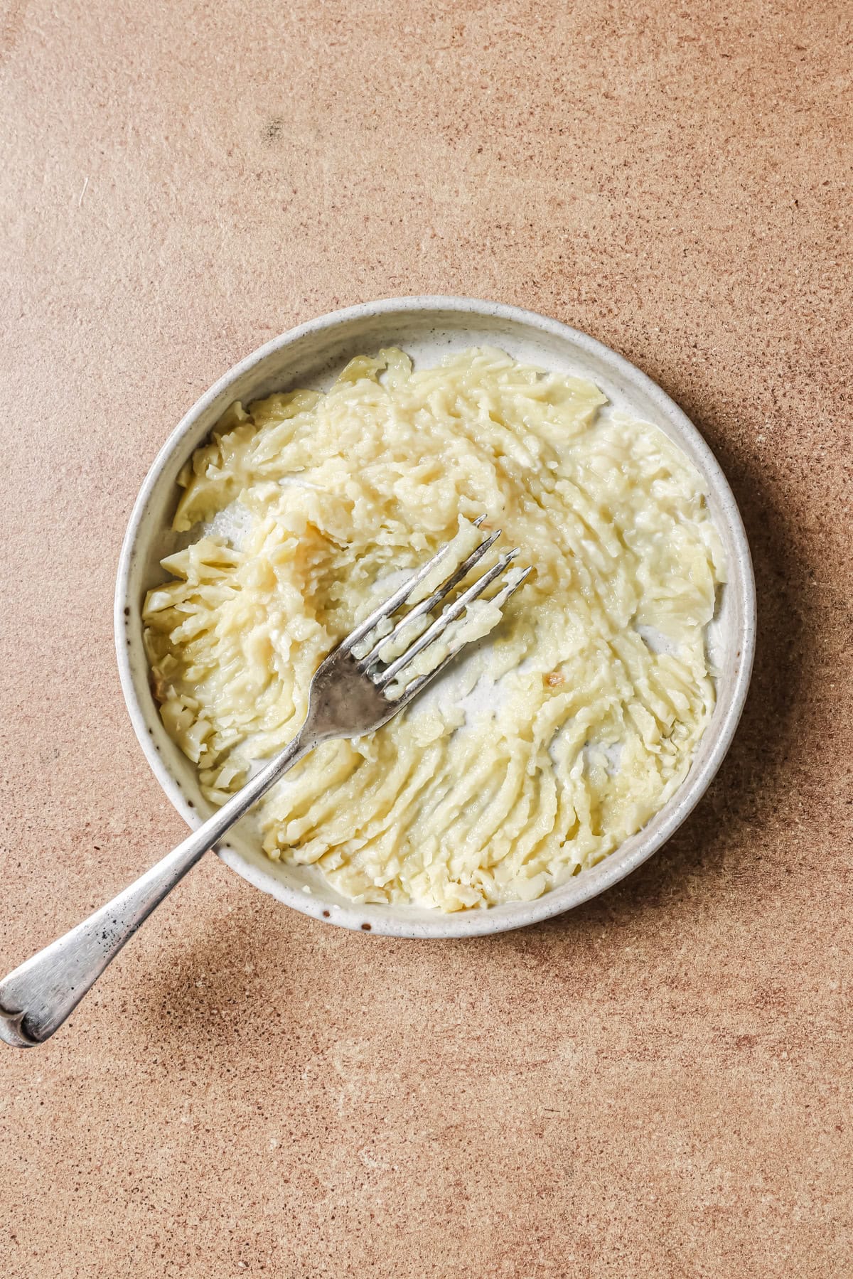 A silver fork resting in a small, shallow bowl of mashed potatoes.