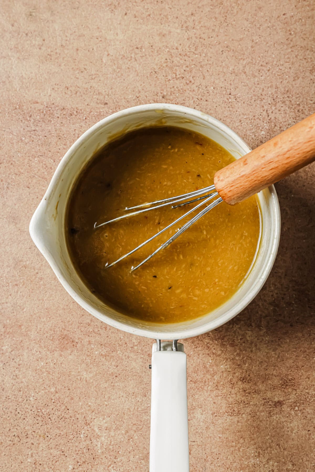 A metal whisk resting in a saucepan filled with a golden-brown sauce.